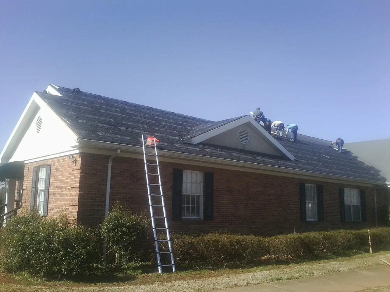 Crew tearing shingles off a brick ranch roof with a ladder set — Emergency Roof Repair work by our crew in Artois