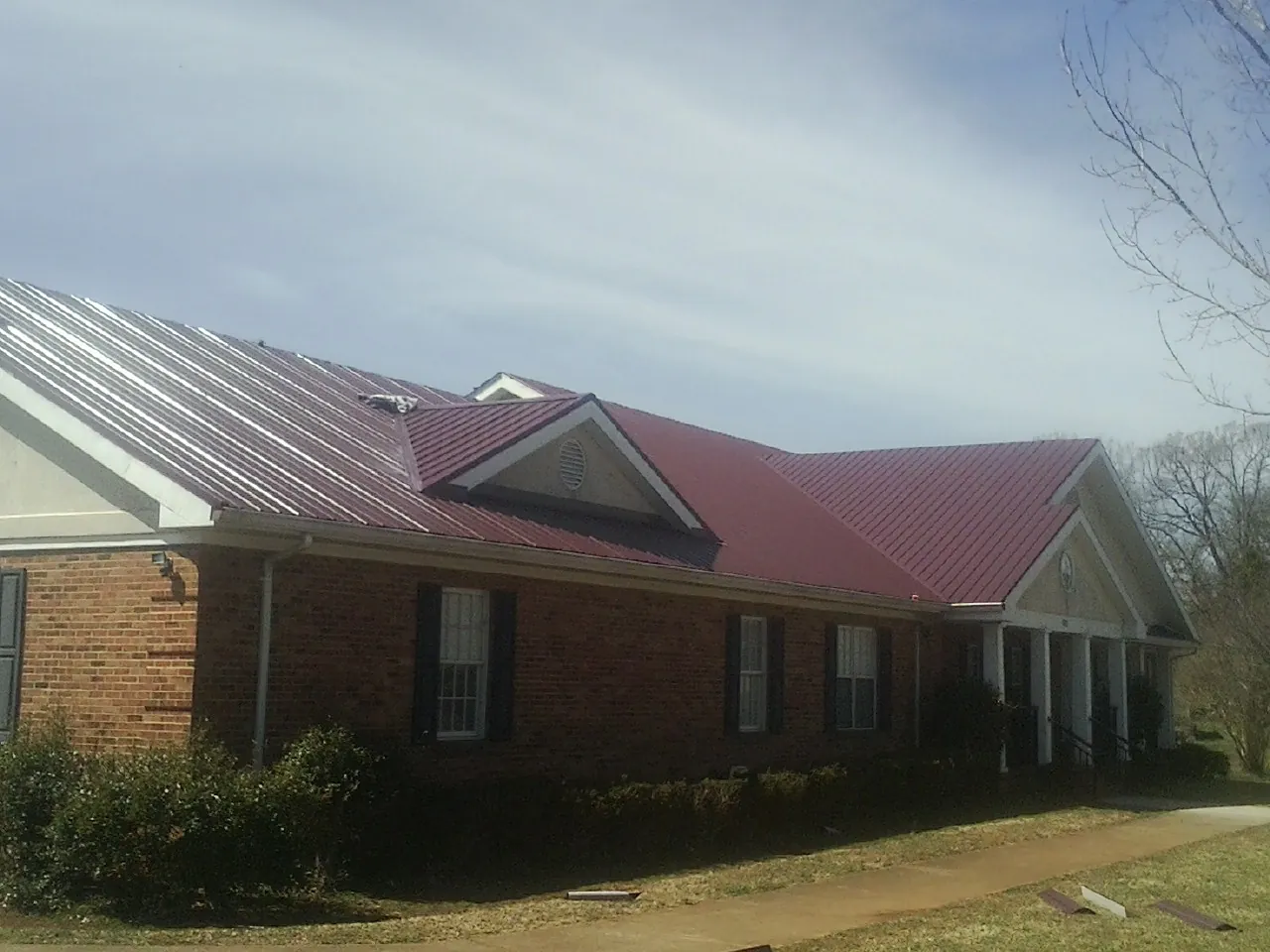 Red metal roof with gabled entries on a long brick building, from a Hail Damage Roof Repair job in Artois