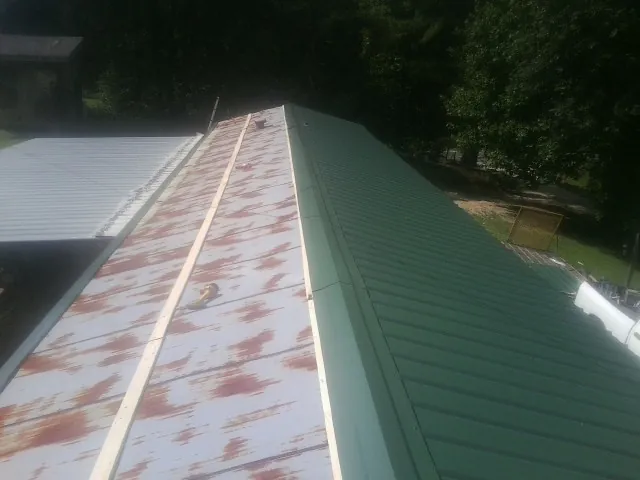Old rusted panels beside newly installed green metal roofing — Wind Damage Roof Repair by Roofing Brothers in Artois