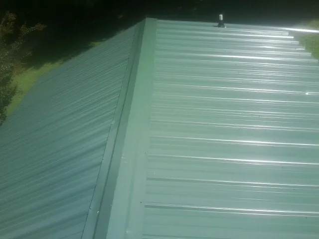 New green metal panels meeting at the ridge of a roof — Flat Roof Repair work by our crew in Artois