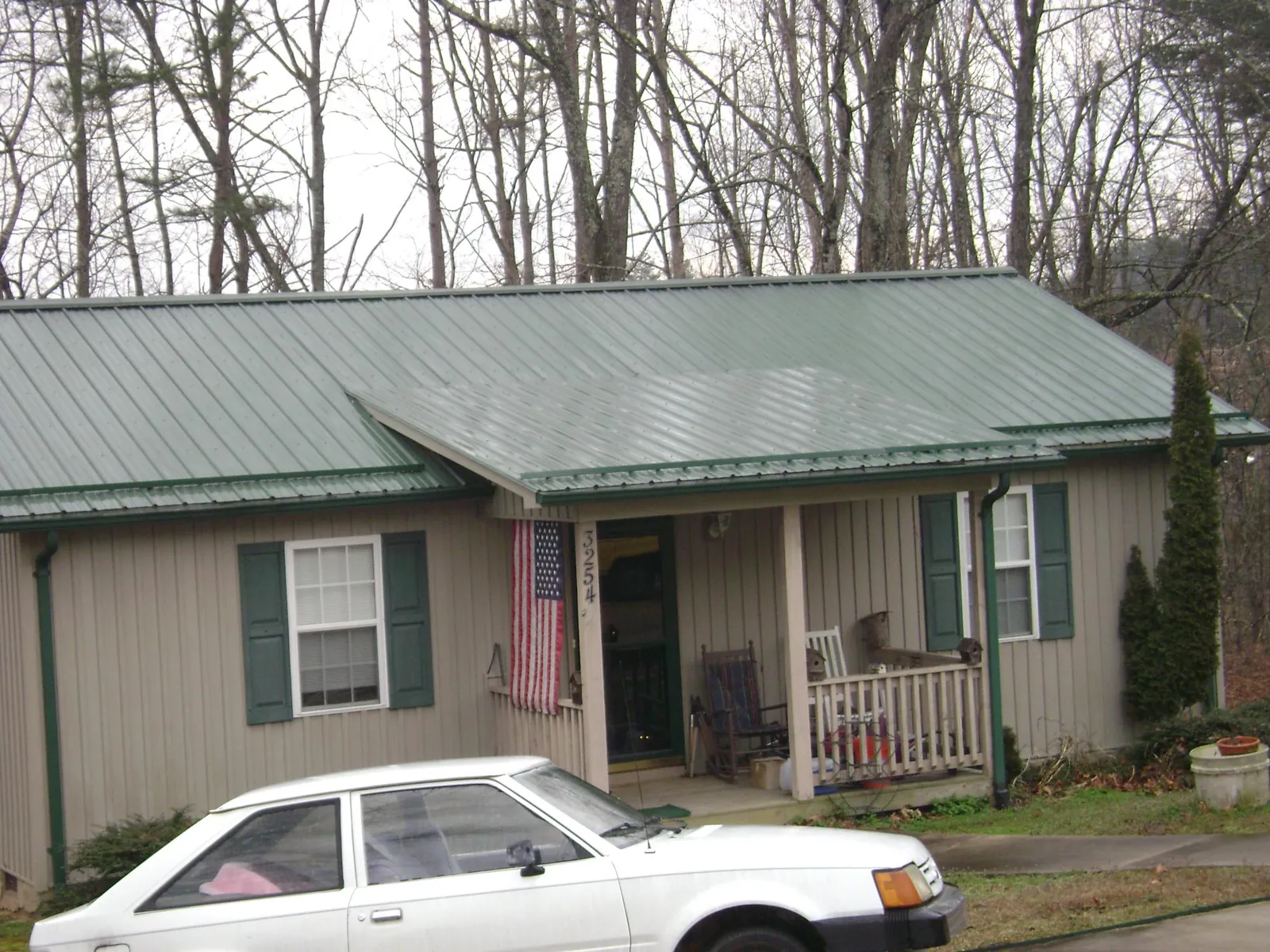 Green metal roof and front porch on a tan sided cottage in Artois